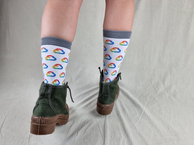 May include: A pair of green ankle boots with brown soles. The person wearing the boots is wearing white socks with a rainbow cloud pattern.