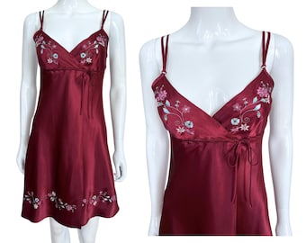 May include: A burgundy satin slip dress with delicate floral embroidery in shades of pink and white. The dress has a V-neckline and adjustable straps.