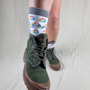 May include: Green canvas high-top boots with brown rubber soles and laces. The boots are worn with white socks featuring a colorful cloud pattern.