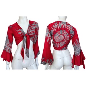 Puede incluir: Top corto rojo con lazo y mangas acampanadas largas. El top presenta un estampado tie-dye gris en las mangas y la parte delantera. La parte trasera del top tiene un diseño tie-dye en espiral gris. El top se muestra en un maniquí.