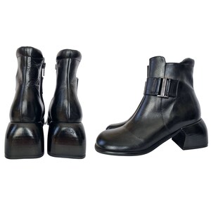 Pode incluir: Par de botas de tornozelo de couro preto com salto grosso e detalhe de fivela no tornozelo. As botas têm um zíper no interior de cada bota.