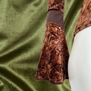 May include: A brown velvet top with long sleeves and a bell-shaped cuff. The sleeves have a brown fabric band at the wrist.