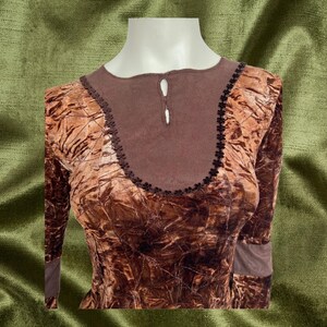 May include: A brown velvet top with a textured pattern and a brown knit neckline. The neckline has a small keyhole opening with a button closure.