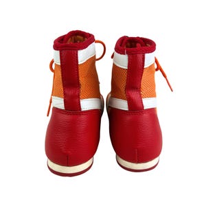 May include: A pair of red and orange boxing shoes with white accents. The shoes have a high top design and are laced up.