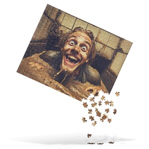 May include: A jigsaw puzzle featuring a person covered in mud, with a wide-eyed expression and open mouth. Some puzzle pieces are falling away from the main image, creating a dynamic visual.