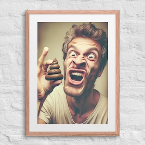 May include: Framed print featuring a man with an exaggerated expression of disgust, holding a small, brown, sculpted object resembling feces. The man is wearing a white t-shirt. The artwork is framed in a light brown wooden frame.