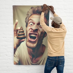 May include: A wall tapestry featuring a close-up of a man with an exaggerated expression, holding a stack of brown objects. A person is hanging the tapestry on a white brick wall. The man's face is contorted in a grimace.