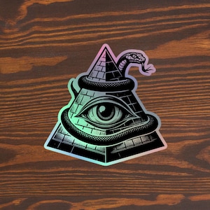 May include: A black and white illustration of an all-seeing eye inside a pyramid, with a snake wrapped around it. The image has a holographic finish.