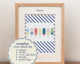 May include: A complete cross stitch kit featuring a framed pattern of colorful buoys. The kit includes a pattern, needle, 11 ct. aida cloth, threads, and a project bag. The framed artwork displays the word buoys above a row of eight nautical buoys.