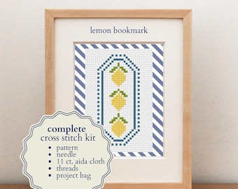 May include: A complete cross stitch kit for a lemon bookmark, framed in light wood. The pattern features three yellow lemons with green leaves in a blue-bordered design. Text reads: lemon bookmark and complete cross stitch kit, pattern, needle, 11 ct. aida cloth, threads, project bag.