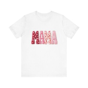 Könnte beinhalten: Weißes T-Shirt mit dem Wort "MAMA" in einem farbenfrohen Design zum Valentinstag. Die Buchstaben sind rot, rosa und weiß mit Herz- und "XOXO"-Mustern. Das Shirt besteht aus einem weichen, bequemen Material.