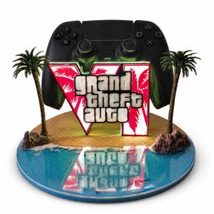 May include: A black video game controller stand featuring a Grand Theft Auto VI logo with palm trees on a circular base. The base depicts a sandy beach meeting blue water with a reflective surface, and the logo is illuminated from behind.