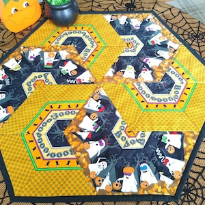 May include: A hexagonal table runner with a black and yellow geometric pattern featuring ghosts, pumpkins, and the word "BOO" repeated throughout.