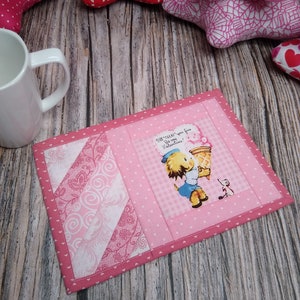 May include: Pink and white quilted coaster with a pink gingham border and a vintage Valentine's Day illustration of a girl holding a heart-shaped ice cream cone. The text on the illustration reads "Sweet Treat! You're fine to my Valentine!"
