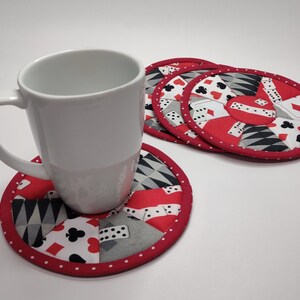 May include: Four red and white fabric coasters with a design of playing cards and dice. A white ceramic mug is sitting on one of the coasters.