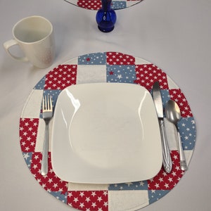 May include: A white ceramic plate with a silver fork and spoon, set on a red, white, and blue star-patterned placemat.
