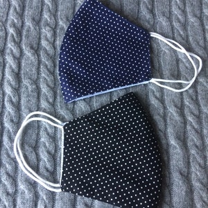 Puede incluir: Dos mascarillas con lunares blancos sobre un fondo oscuro. Una mascarilla es azul marino y la otra es negra.