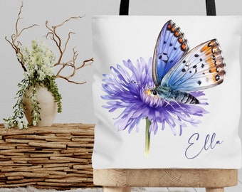 Könnte beinhalten: Eine weiße Einkaufstasche mit einer Aquarell-Illustration eines blauen Schmetterlings auf einer lila Blume. Die Tasche trägt den Namen "Ella" in Kursivschrift in der unteren rechten Ecke.