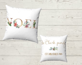 May include: Two white throw pillows with gold lettering and floral accents. The larger pillow says "NOEL" and the smaller pillow says "The Clark family established 2015".