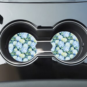 May include: Two round car coasters with a blue and green floral pattern. The coasters are in a car cup holder.