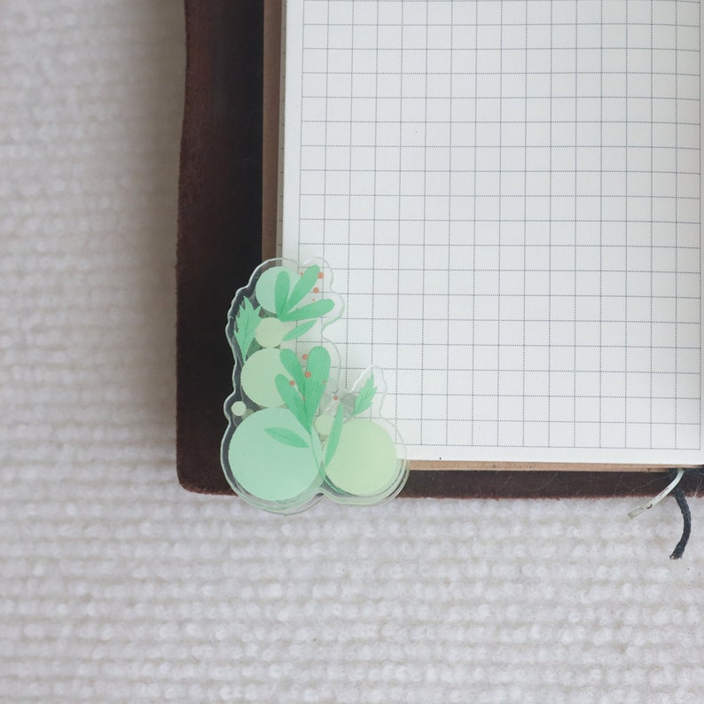 May include: A green and white floral sticker with a layered design. The sticker features a cluster of leaves and rounded shapes.