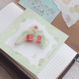 May include: A clear plastic sticker with a cherry design. The sticker is on a green and white background with the text "&copy;Raccoon Cap" in the bottom right corner.