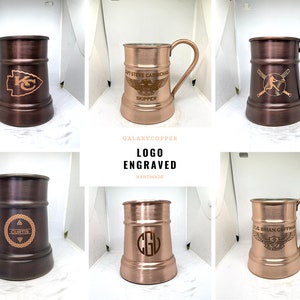 May include: Six copper mugs with different logos engraved on them. The mugs are all the same size and shape, and they have a hammered finish. The logos include a baseball player, a football team logo, a monogram, and a winged logo with text. The mugs are all on a white background.