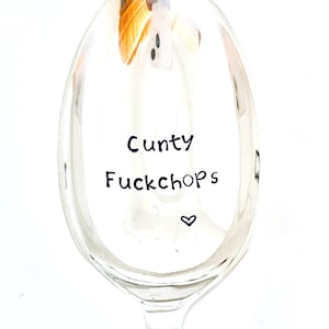 以下が含まれることがあります： スプーンのボウル部分の中央に黒いスタンプで「Cunty Fuckchops」という文字が刻印された、光沢のある銀色の金属製スプーン。文字のすぐ下には、反射する表面に小さな黒いハートのシンボルがスタンプされています。