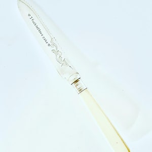 May include: A silver cake knife with a white handle. The blade has a decorative design and the words "I fucking love cake" engraved on it.