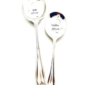 May include: Two silver spoons with handles. The larger spoon says "Big Spoon" and the smaller spoon says "Little Spoon".