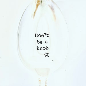 Puede incluir: Una cuchara de plata con el texto "Don't be a knob" escrito en ella. Una pequeña estrella está dibujada al lado del texto.