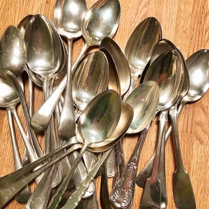 Puede incluir: Un montón de cucharas de plata vintage con mangos ornamentados. Las cucharas están dispuestas en un patrón aleatorio, con algunas superpuestas. Las cucharas están todas pulidas y brillantes.