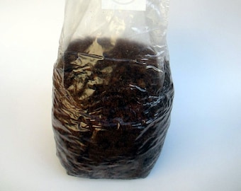 May include: A clear plastic bag filled with dark brown soil. The bag has a white circle label with a blank space in the center.