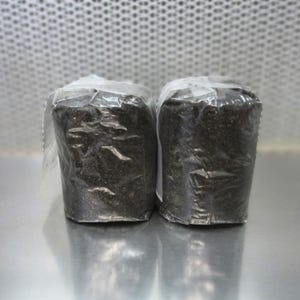 May include: Two black, rectangular, wrapped packages, likely containing soil or potting mix, are sitting on a silver surface.