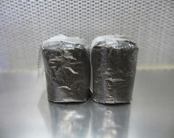 May include: Two black, rectangular, wrapped packages, likely containing soil or potting mix, are sitting on a silver surface.