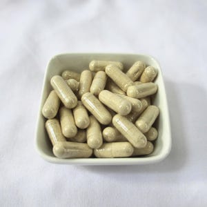 May include: A white ceramic bowl filled with beige capsules. The capsules are arranged in a random pattern.