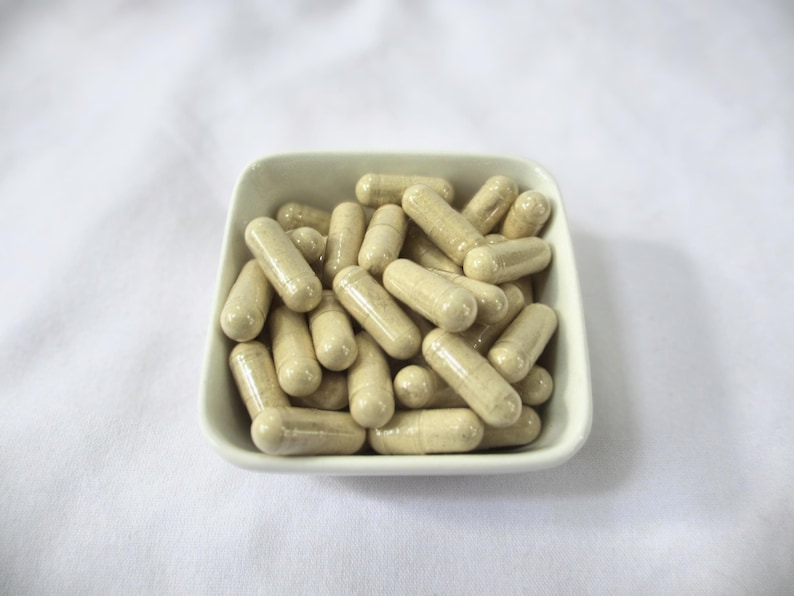 May include: A white ceramic bowl filled with beige capsules. The capsules are arranged in a random pattern.