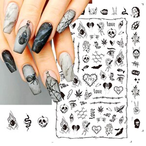 May include: Black and white nail art stickers with various designs including hearts, skulls, spiders, eyes, and the word "love".