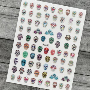 May include: A sheet of colorful sugar skull nail art stickers. The stickers feature various designs with vibrant colors and patterns, including flowers, hearts, and geometric shapes. The text "WG660" is printed on the sheet.