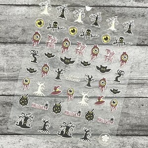 May include: Clear sheet of Halloween-themed nail art stickers. Designs include bats, witch hats, eyeballs, skulls, trees, and cauldrons. Text includes "Trick or Treat" and "Halloween".