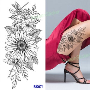 Pu&ograve; includere: Disegno di tatuaggio temporaneo in bianco e nero con un girasole con accenti di libellula. Il design del tatuaggio &egrave; mostrato sulla gamba di una persona.