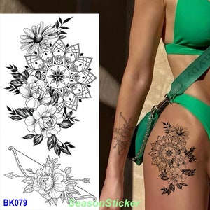 Pu&ograve; includere: Tatuaggio temporaneo in bianco e nero con un design a mandala, fiori e una freccia. Il tatuaggio &egrave; mostrato sul braccio e sulla coscia di una persona.