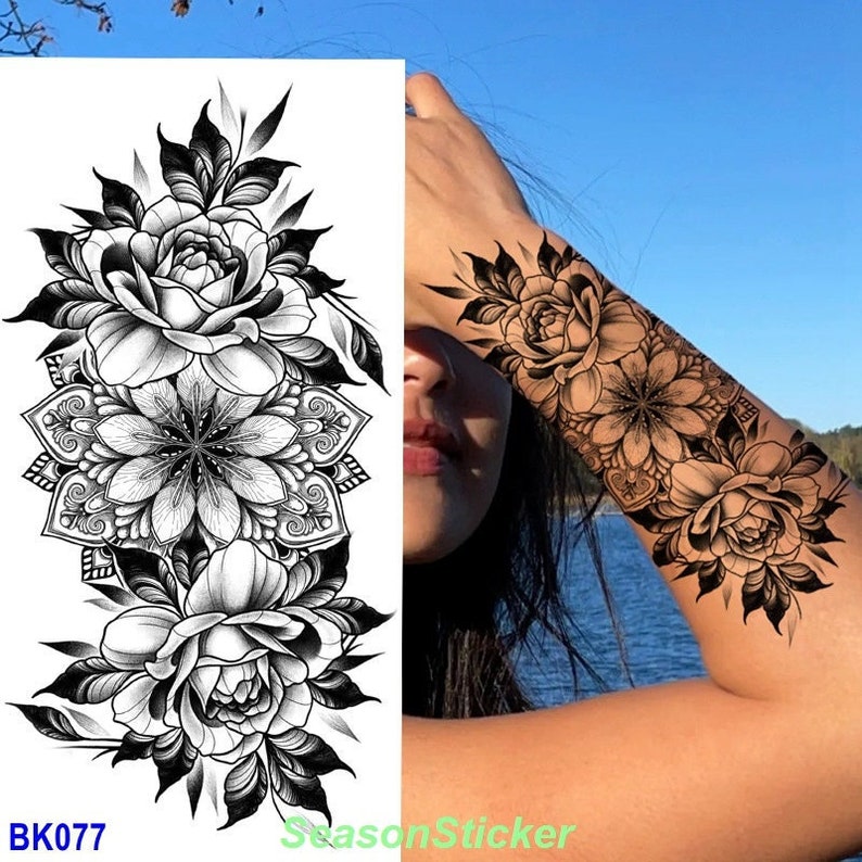 Pu&ograve; includere: Tatuaggio temporaneo in bianco e nero con un grande disegno di mandala e due rose su entrambi i lati. Il tatuaggio &egrave; mostrato applicato sul braccio di una persona.