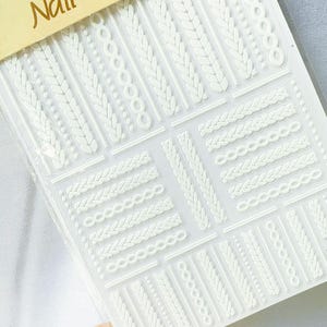May include: A sheet of white nail art stickers featuring various textured designs, including braided patterns and linked circles. The word "Nail" is visible at the top. These stickers offer a decorative element for nail art.