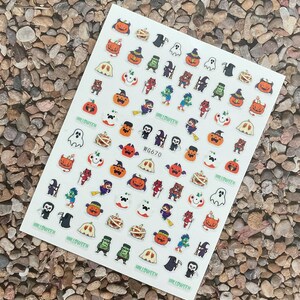 May include: A sheet of Halloween-themed nail art stickers. The stickers feature various spooky characters and objects, including pumpkins, ghosts, mummies, and witches. The word "HALLOWEEN" is printed on the stickers. The product code "WG670" is also printed on the sheet.