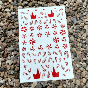 Può includere: Un foglio di carta adesiva bianca con disegni di bastoncini di zucchero e menta rossa e bianca. Il foglio include diversi disegni di bastoncini di zucchero e vortici di menta.