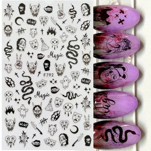 May include: A sheet of black and white nail art stickers featuring a range of designs, including skulls, snakes, demons, and crosses. The stickers are on a clear background and are ready to be applied to nails. The sheet also includes the text "Magic" and "F792".