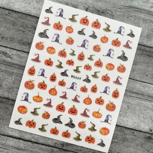 May include: A sheet of Halloween-themed nail art stickers. The stickers feature orange pumpkins with various carved faces, witch hats in black, green, and purple, and wizard hats. The text "WG669" is printed on the sheet.