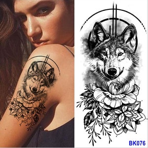 Pu&ograve; includere: Tatuaggio temporaneo in bianco e nero con la testa di un lupo e un design floreale. Il lupo &egrave; circondato da un cerchio con un design geometrico. Il tatuaggio &egrave; sulla spalla di una persona.