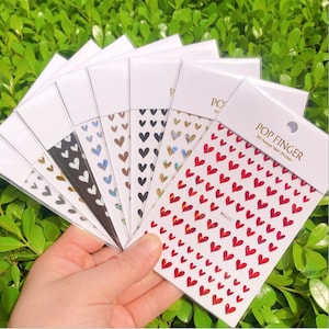 May include: A set of 10 sheets of 3D nail art stickers featuring a variety of heart designs. The stickers are holographic and come in different colors, including red, gold, silver, black, and white.